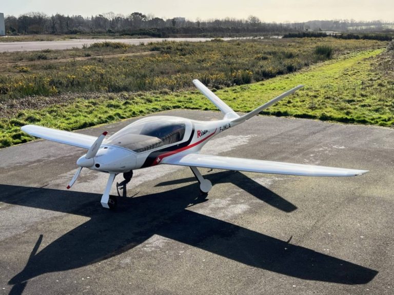 Small white airplane parked on tarmac near grass.