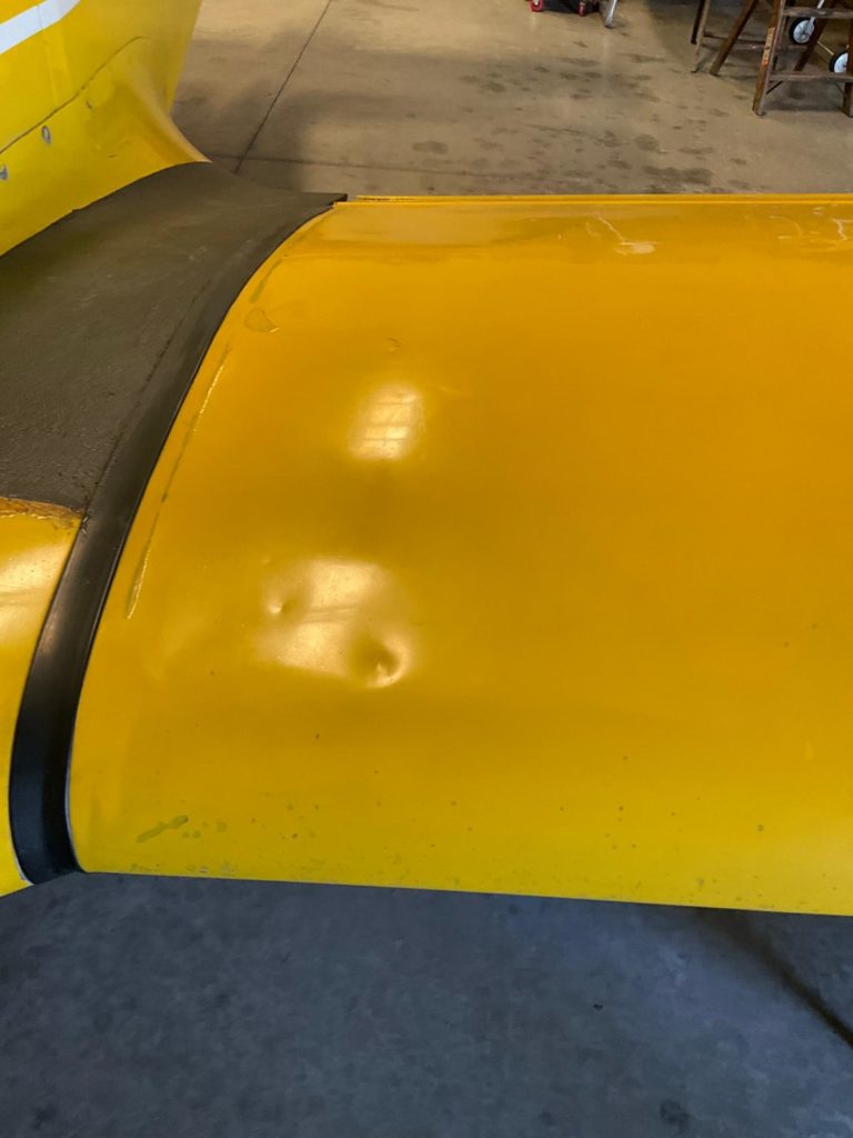 Yellow aircraft wing with visible dents in hangar.