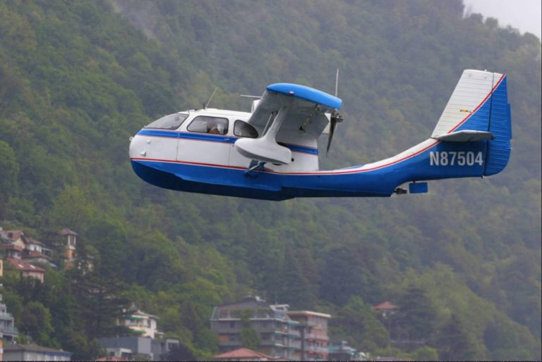Blue seaplane flying over forested hills
