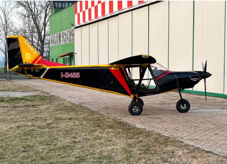 Colorful light aircraft parked by hangar.
