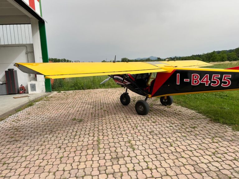 Bright yellow small plane parked on grassy pavement.