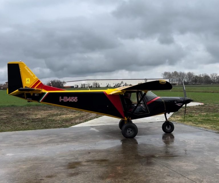 Small airplane parked on wet runway, cloudy sky.