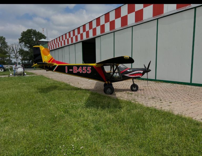 Colorful small aircraft parked near hangar.