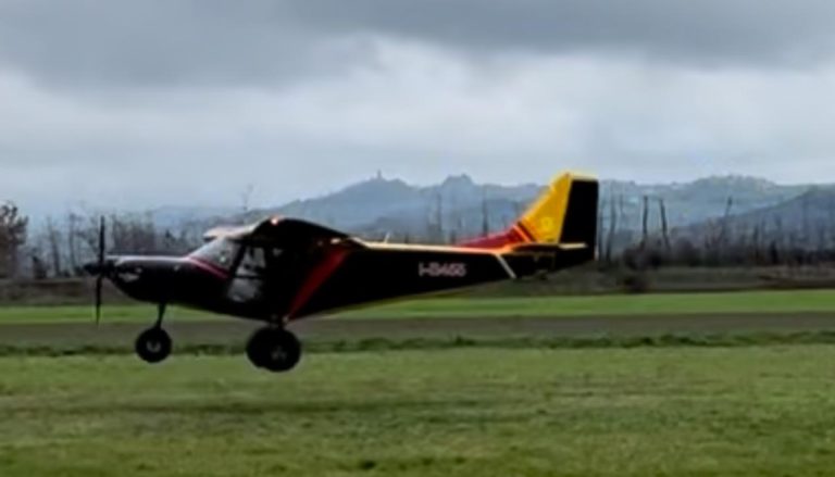 Small airplane landing on grass runway under cloudy skies.