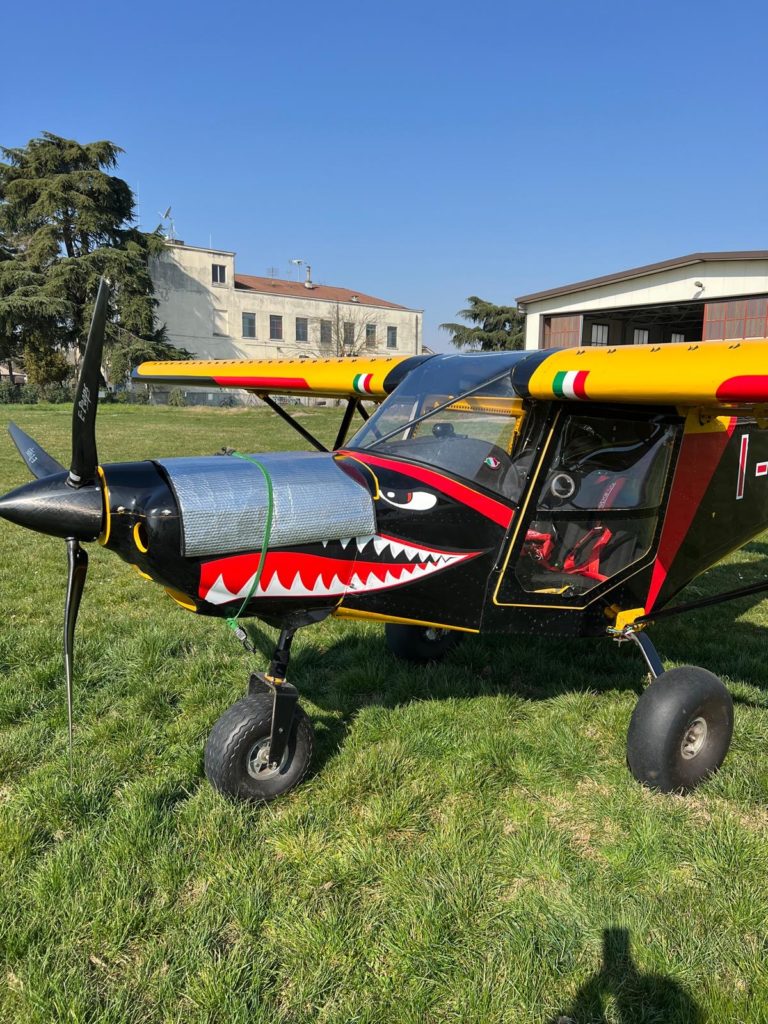 Small colorful aircraft with shark mouth design on grass.