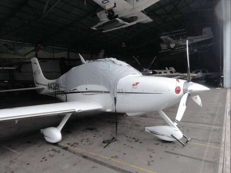 White small aircraft in hangar with cover on.