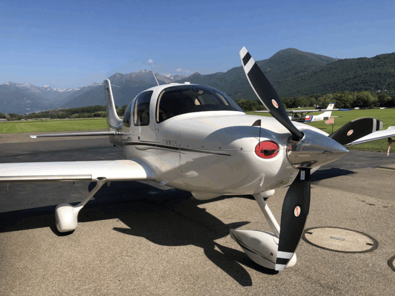 Small propeller airplane parked on airstrip with mountains.