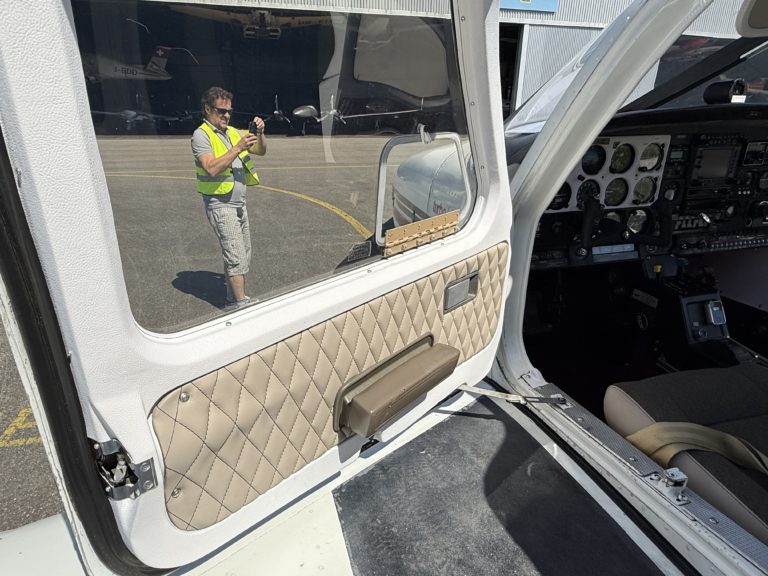 Person photographing airplane cockpit reflection through open door.