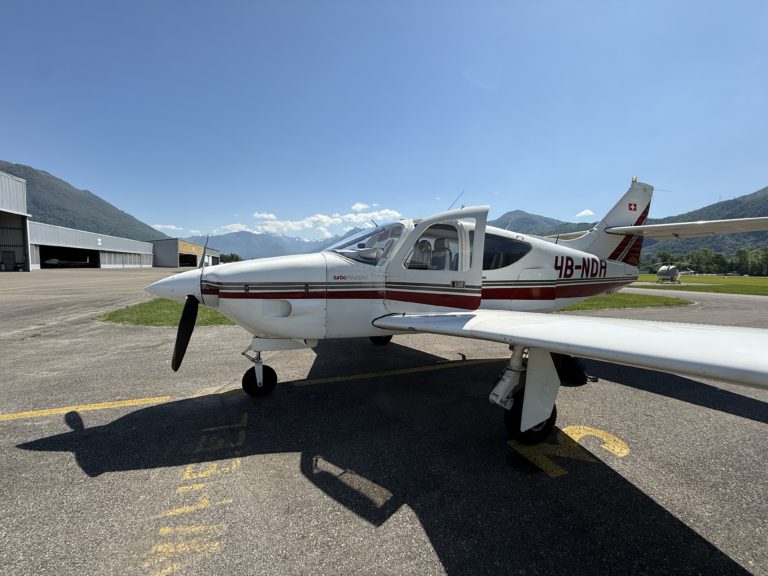 White airplane parked on sunny airfield with mountains.