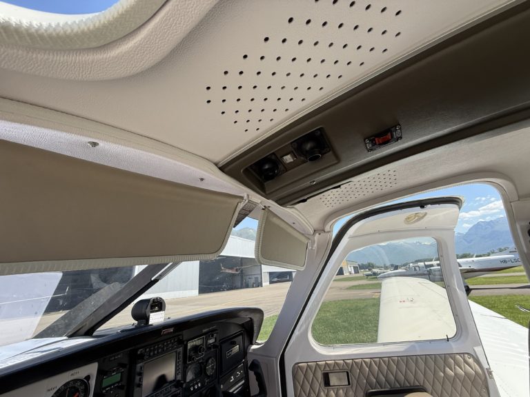 Cockpit interior view with open door, mountainous backdrop.