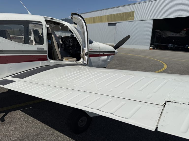 Small aircraft parked near hangar with open door.