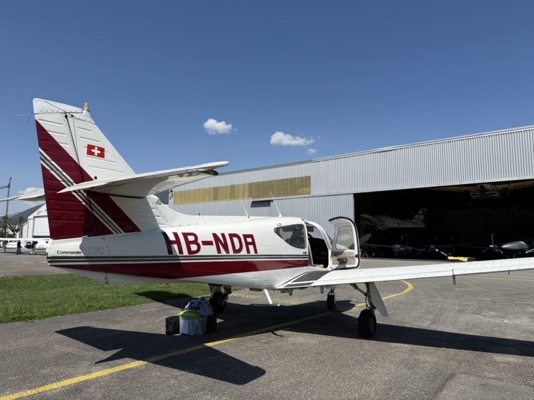 Small plane parked outside hangar on sunny day.