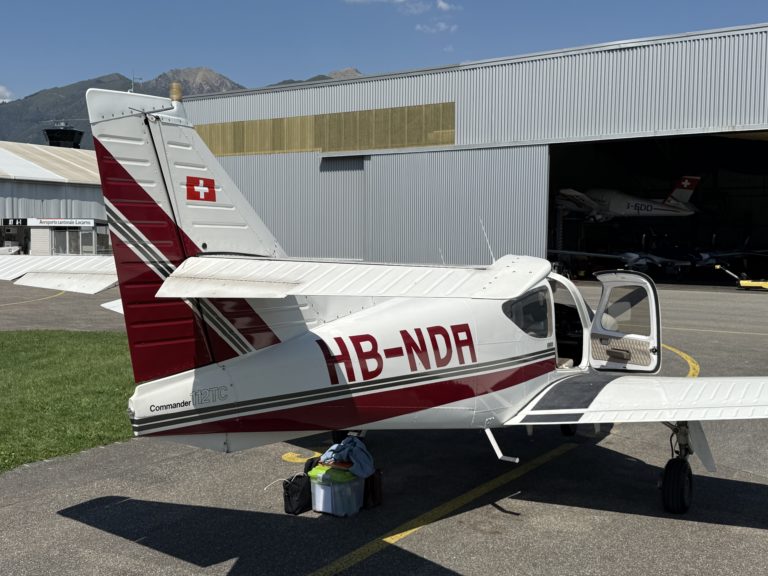 Small Swiss airplane parked near hangar entrance.