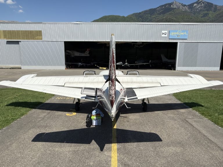 Small airplane parked outside hangar on sunny day.