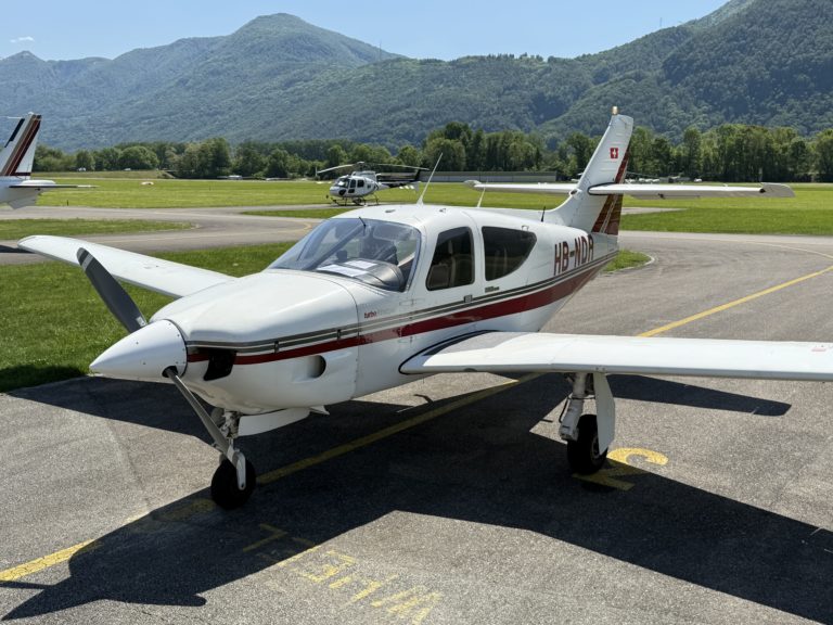 Small airplane parked on airport runway with mountains.
