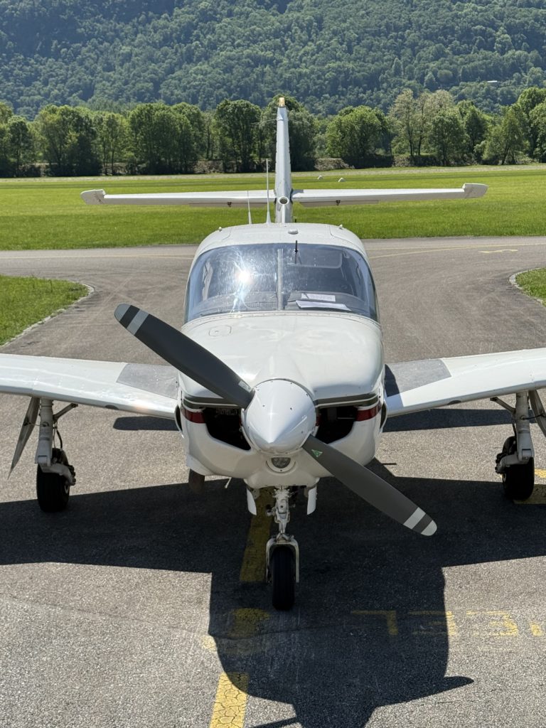 Small airplane on runway with green trees backdrop.