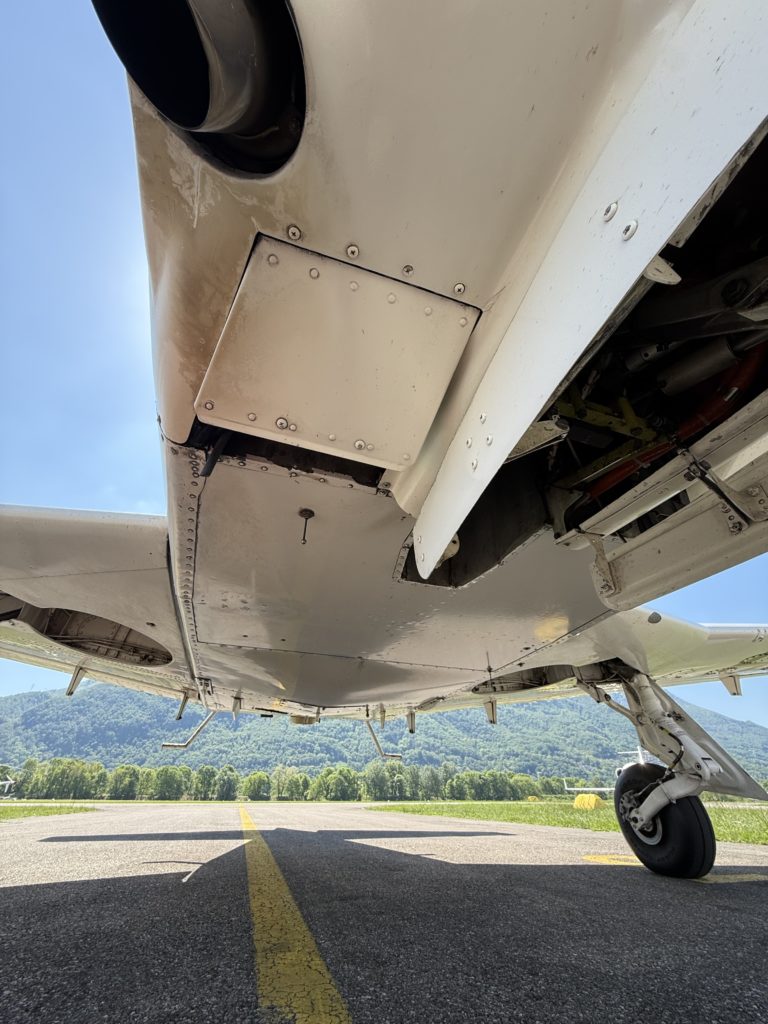 Aircraft undercarriage with runway and mountains view.