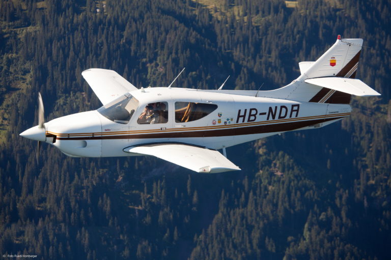 Small airplane flying over forested mountains.