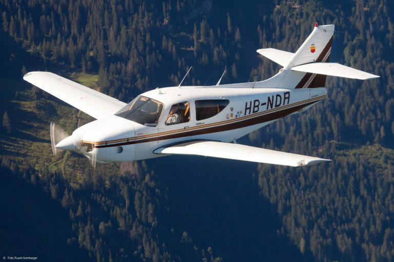 Small plane flying over forested mountains.