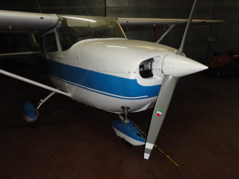 Small white and blue propeller airplane in hangar.
