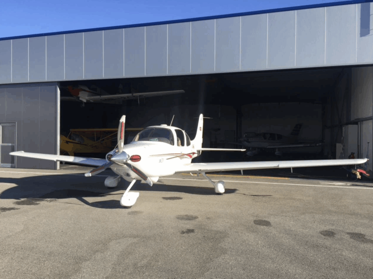 Small airplane parked outside hangar on sunny day.